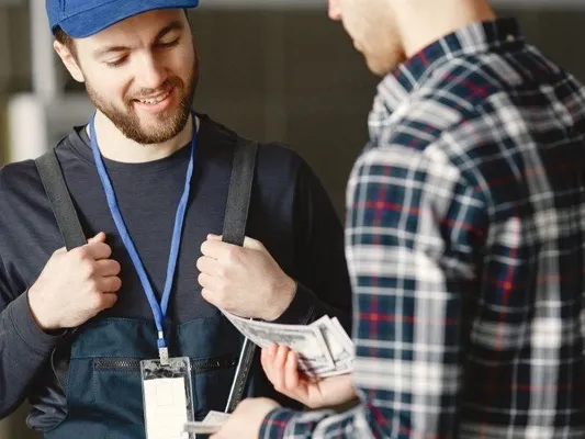 Customer handing cash to a smiling technician in a cap and overalls