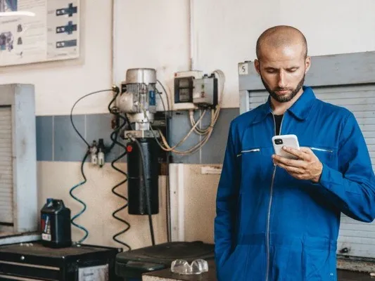 Technician in blue coveralls reading his phone in a workshop